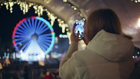 girl taking photo ferris wheel on cellphone at night amusement fair closeup