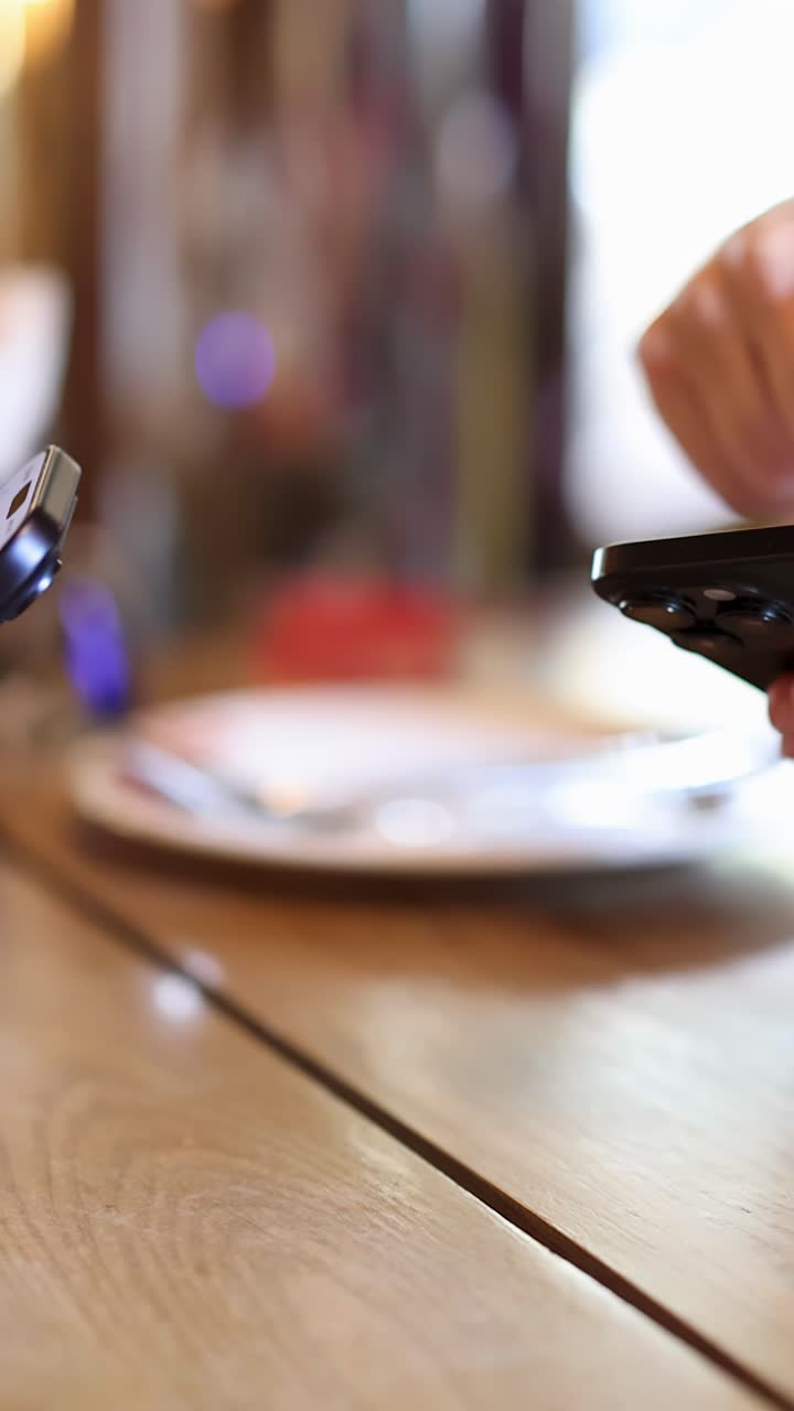 Person interagerer med mobil enhed ved spisebordet, skarpt indendørs lys, lav dybdeskarphed.