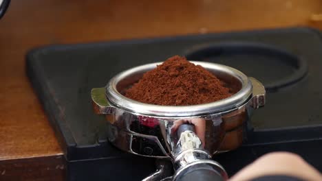 close-up of a barista tampering coffee grinds in a portafilter before brewing coffee in a caf?