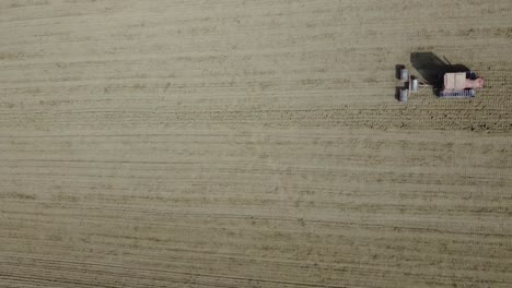 aerial top down of red tractor with triple roll equipment plowing and preparing the agricultural soil for the seeding in natural organic farming