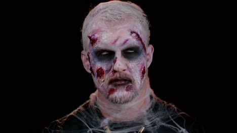 aterrador espeluznante muerto viviente herido hombre halloween zombie haciendo caras, mira a la cámara y sonríe terriblemente