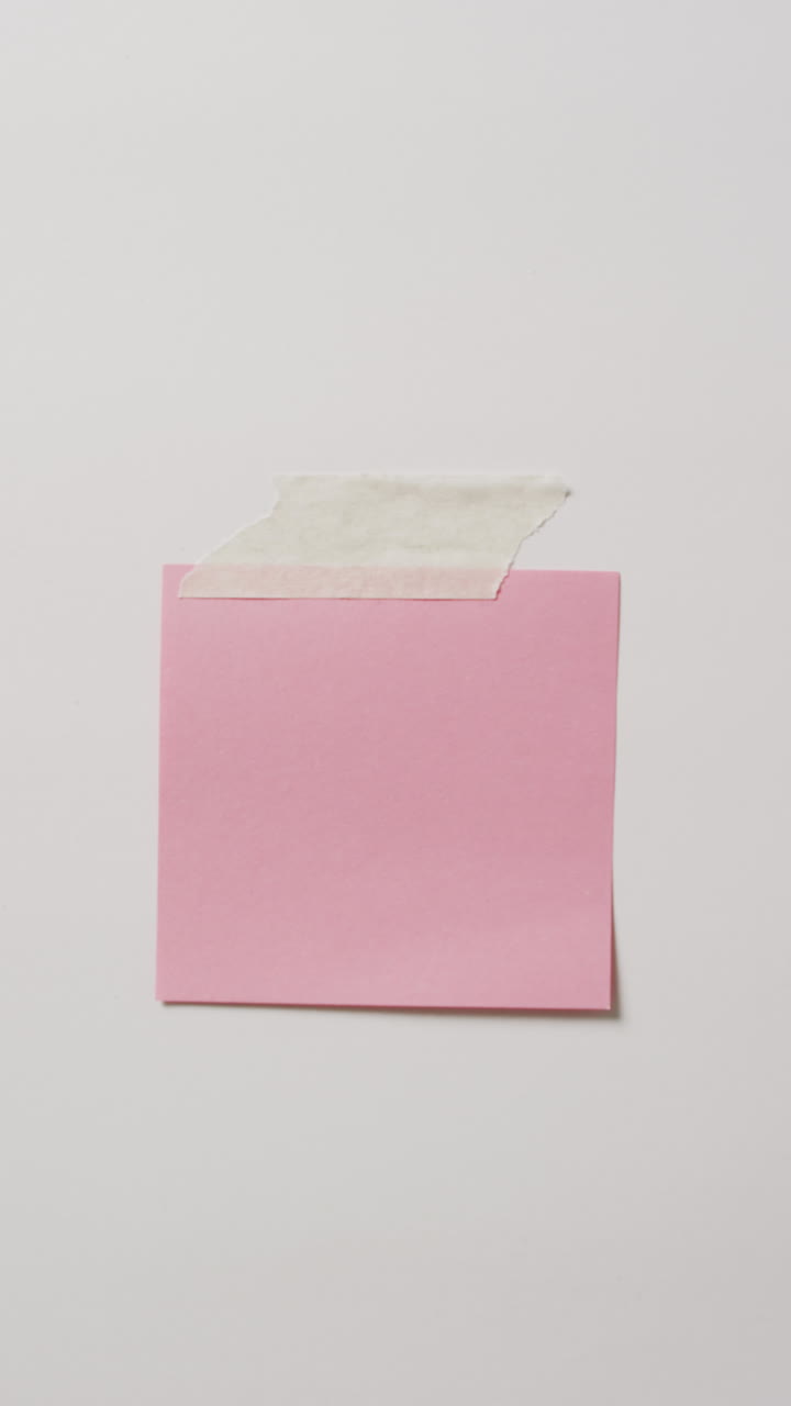 Vertical video of close up of pink memo note taped to white background with copy space
