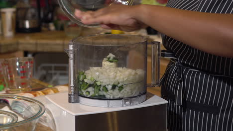 woman pours chopped jalapeno peppers and onions into food processor, closeup