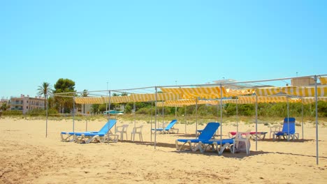 blue lounge and deck chairs at empty beach during covid-19 pandemic on a sunny summer day. - wide shot