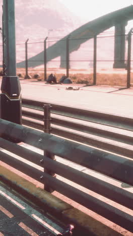 a rusty metal fence along a highway with a bridge in the background