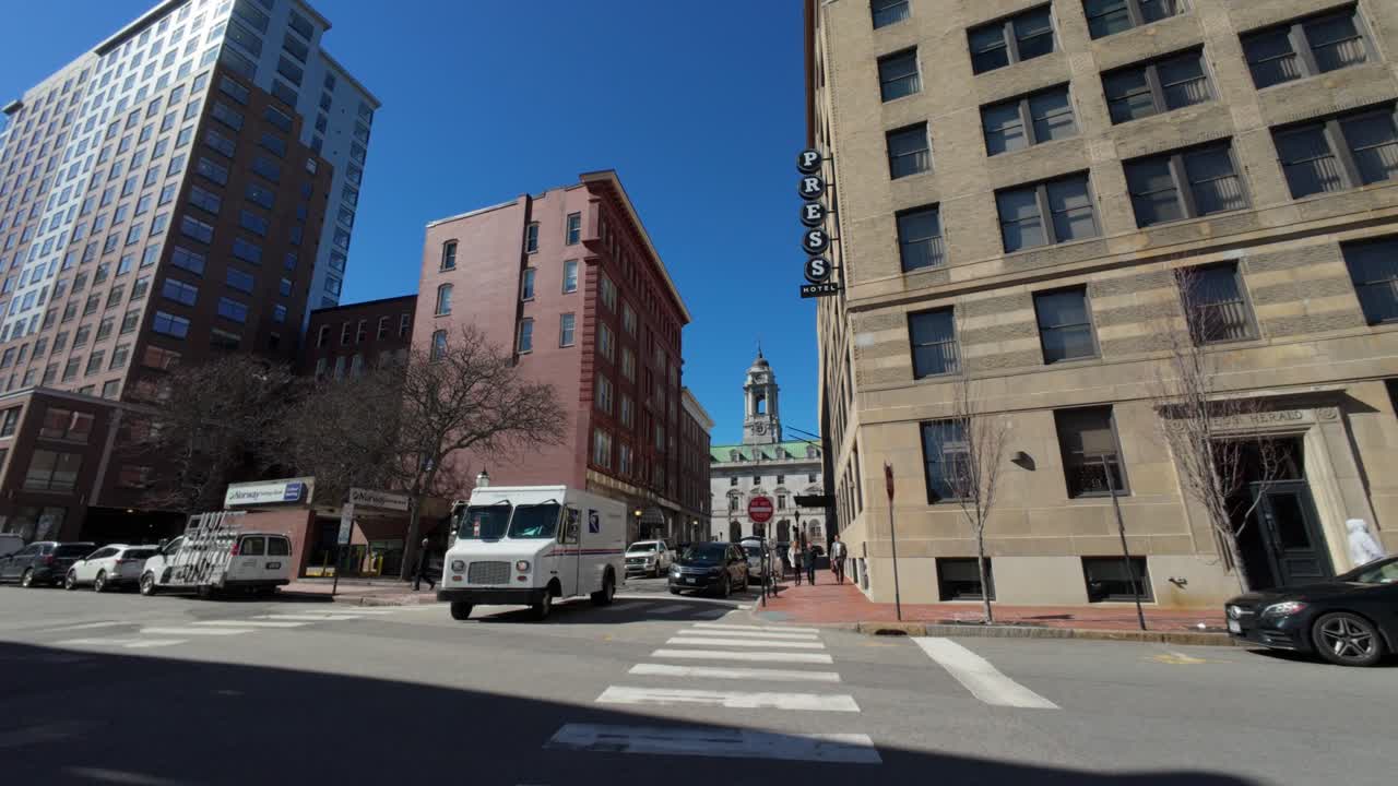 View of stunning high rise building with white truck passing by on street, under clear blue sky in Portland, Maine, USA.