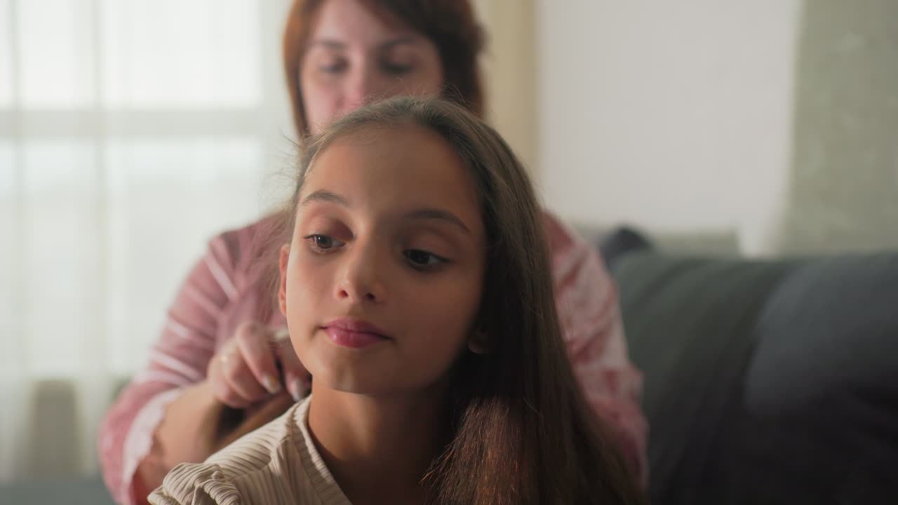Tata che pettina i capelli di una bambina, momento intimo tra assistente e bambino, ambiente domestico informale, cura materna, relax al chiuso, cura personale, tempo felice in famiglia, primo piano.