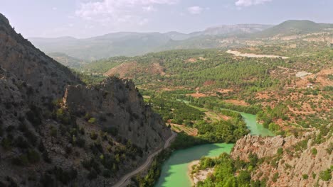 flying above rocky canyon with winding river and sunlit woodlands and fields