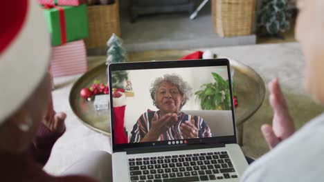 dos amigas mayores diversas que usan una computadora portátil para una videollamada de navidad con una mujer en la pantalla
