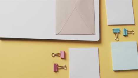 overhead view of notebook, pens and stationery arranged on yellow background, in slow motion