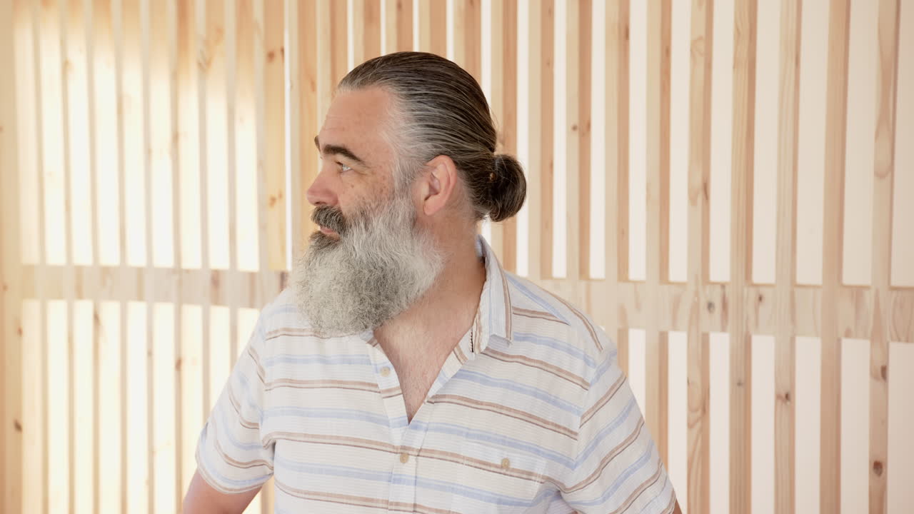 Smiling senior man with beard looking away, wearing striped shirt indoors