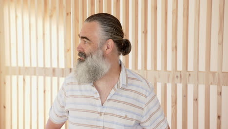 smiling senior man with beard looking away, wearing striped shirt indoors