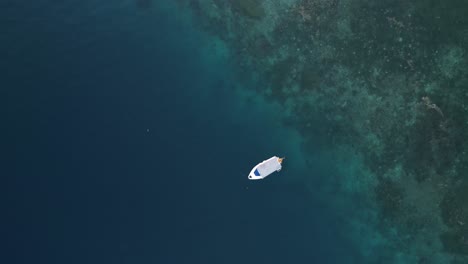 fotografía de un avión no tripulado de un barco flotando en aguas azules con un arrecife de coral visible debajo