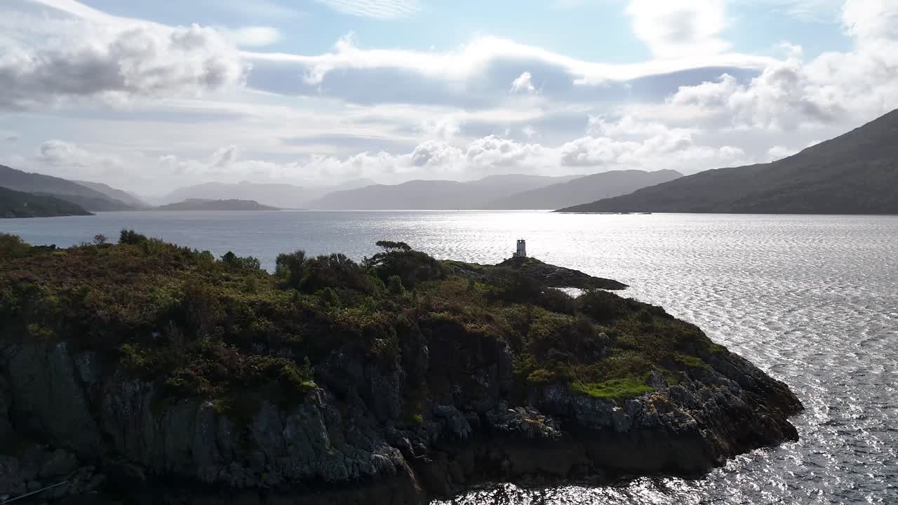 Aerial drone glides toward rugged island with ancient stone tower on Loch Alsh, dramatic sunlight