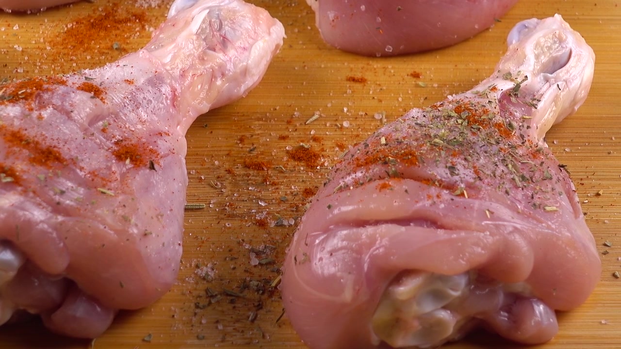 Il processo di marinatura delle cosce di pollo su un tagliere. Il pollo viene cosparso di sale e spezie.