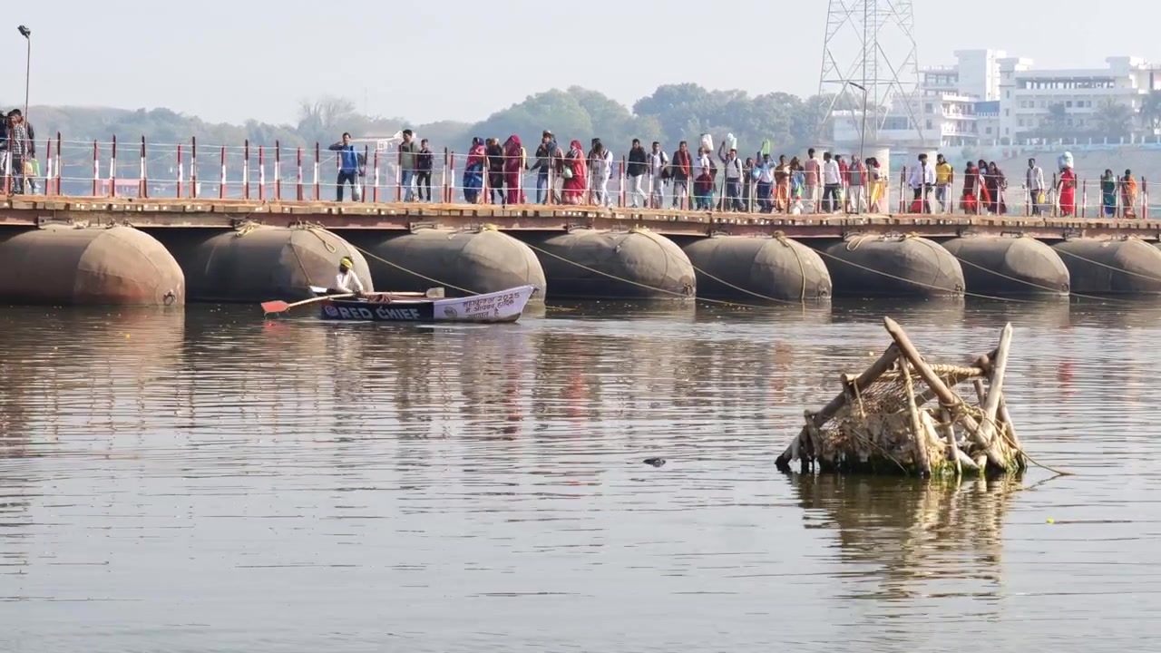 Barcaiolo che manovra una barca a Triveni Sangam con ponte di barche e persone a Prayagraj, Uttar Pradesh, India. Di giorno, ripresa panoramica, 4k
