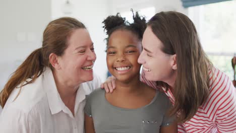 retrato de una feliz pareja de lesbianas caucásicas y su hija afroamericana abrazándose y sonriendo