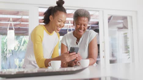 African-american-mother-and-daughter-smiling-while-using-smartphone-together-at-home
