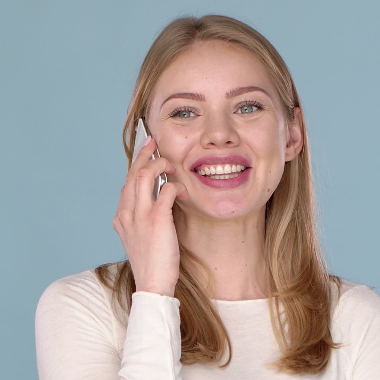 Adorabile giovane donna felice che parla al cellulare. Isolato su uno sfondo blu.