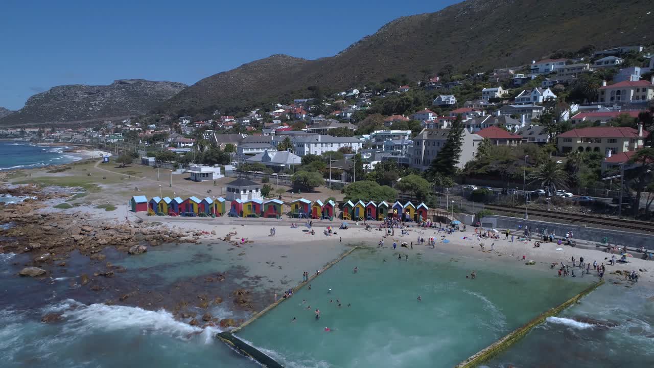 el dron se eleva para revelar cabañas de playa hermosas e históricamente coloreadas de la playa de st james y la piscina de marea del océano con fondo de montaña