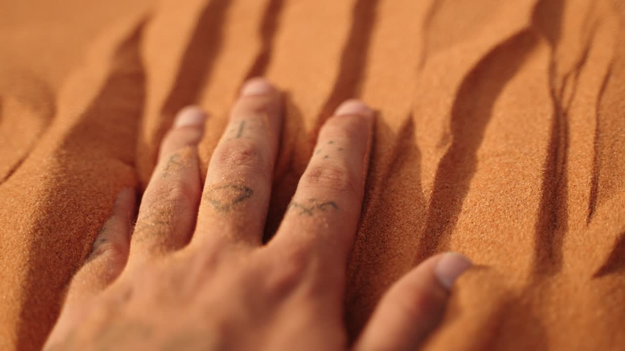 A hand touches soft Sahara sand, leaving imprints shaped by light and shadow