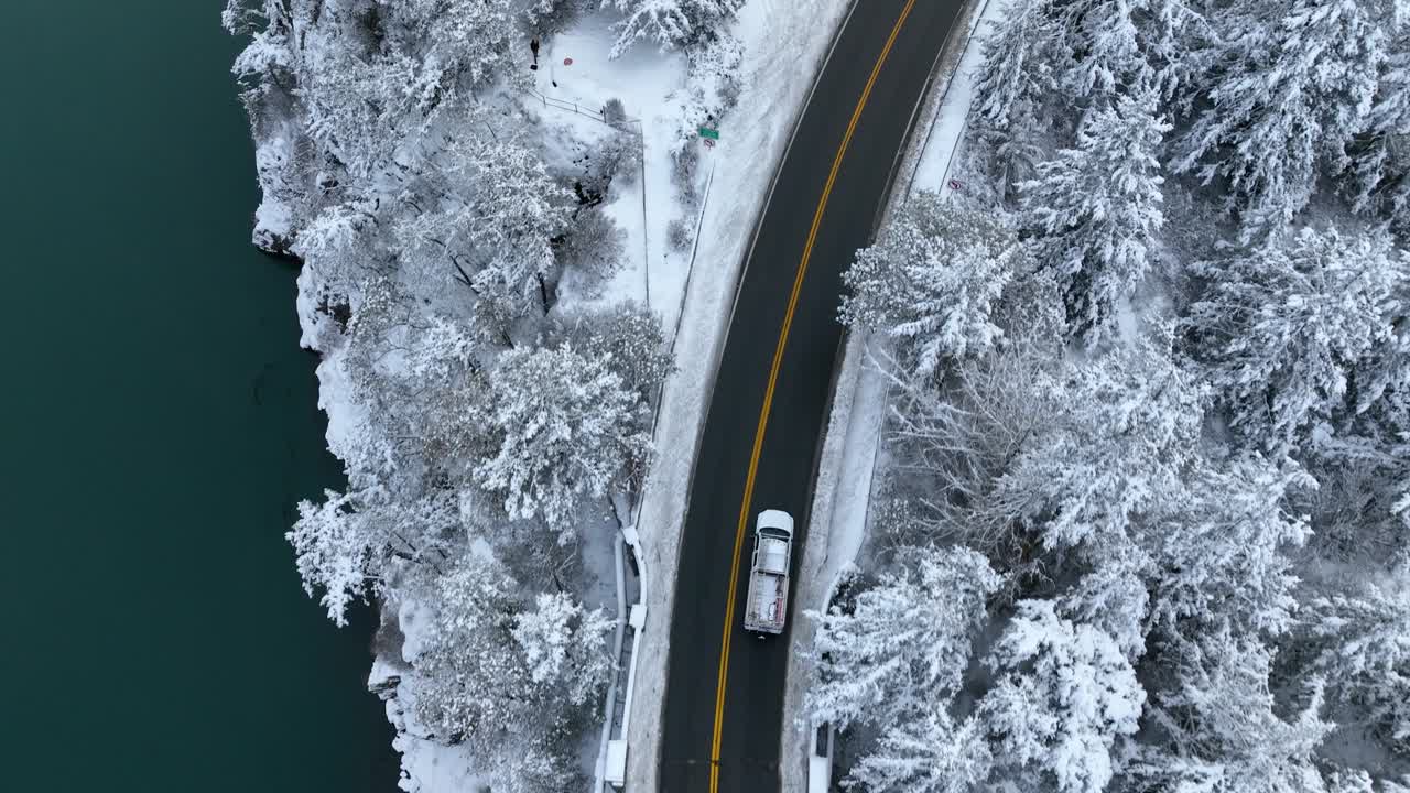 toma de arriba hacia abajo de un camión conduciendo cerca de un cuerpo de agua con nieve cubriendo la tierra
