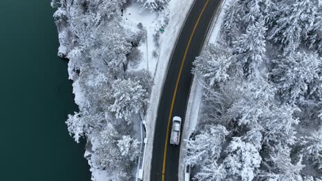 Toma-De-Arriba-Hacia-Abajo-De-Un-Camión-Conduciendo-Cerca-De-Un-Cuerpo-De-Agua-Con-Nieve-Cubriendo-La-Tierra