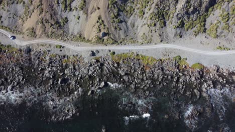 A-birdseye-view-of-a-lone-truck-driving-on-a-gravel-coastal-road