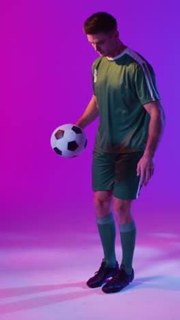 video verticale di un calciatore maschio caucasico con il calcio sopra l'illuminazione rosa al neon