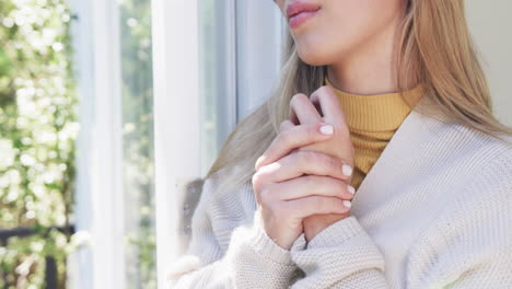 Thoughtful-biracial-woman-looking-through-window-at-home,-slow-motion