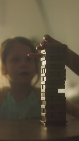 la madre juega juegos de mesa con el niño pequeño alegre hijo e hija sentados en una mesa pequeña en el tiempo libre. la familia se divierte jugando y hablando. la noche de ocio familiar