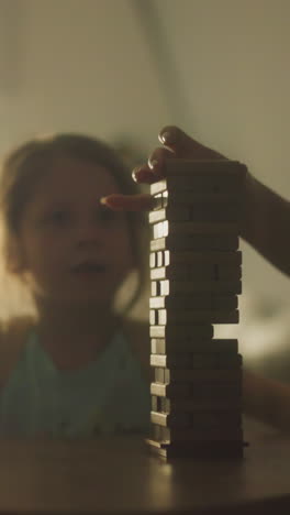 mom plays board games with cheerful toddler son and daughter sitting at small table in free time. family has fun playing and talking. family evening leisure