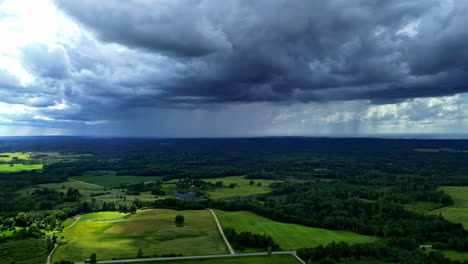 powerful dark rain clouds pouring water over agriculture fields, aerial view