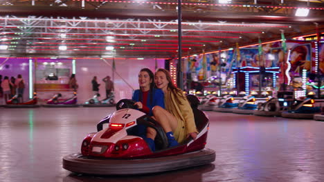 amigos alegres montando un coche de parachoques en luna park. chicas sonrientes conduciendo dodgem.