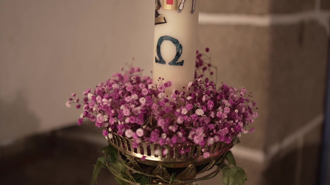 decorated church candle with the Omega symbol, surrounded by pink flowers in a brass holder