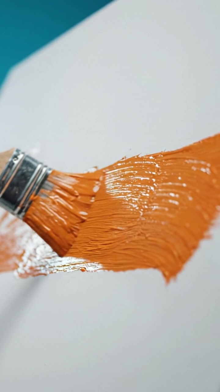 Un primo piano di un pennello che applica pittura arancione vibrante su una tela bianca, catturando il processo artistico e la texture della creatività in azione.