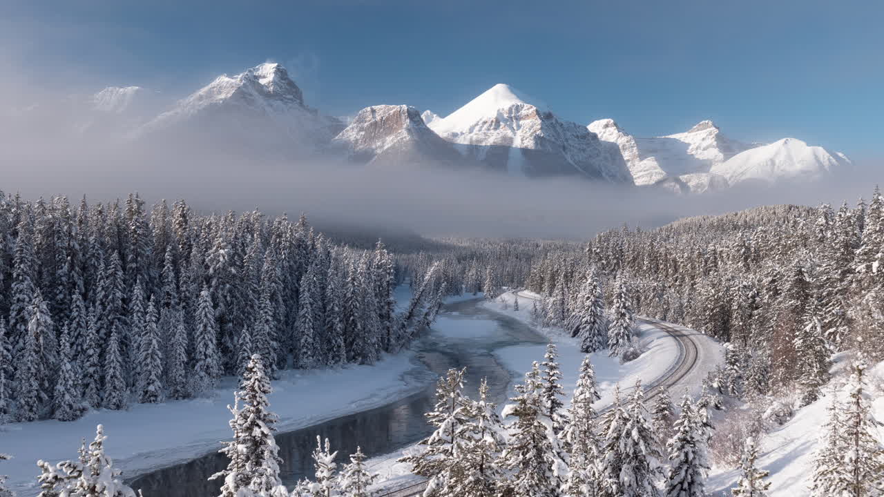 Snowy mountain time-lapse of Morant's curve in Banff National Park which features mountains, forests, a river, and railroad track in a winter wonderland
