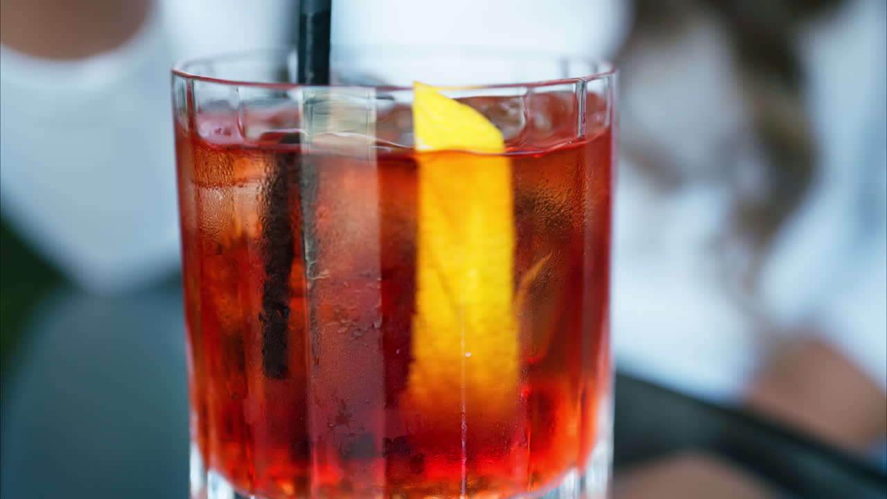 Primo piano di una donna che mescola un cocktail Negroni con una cannuccia