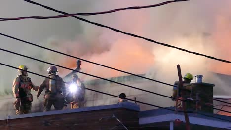 team of firefighters on a roof work together to put out a fire and save people, they are surrounded by smoke from the house