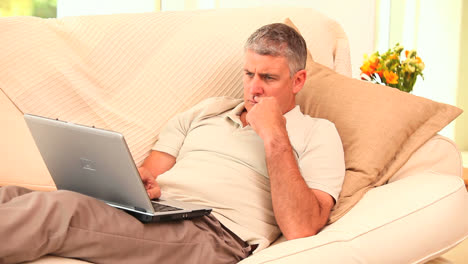 man lying on sofa using laptop
