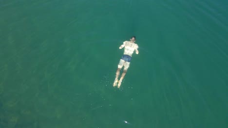 top-down drone footage of a man swimming in a blue lake in the mountains