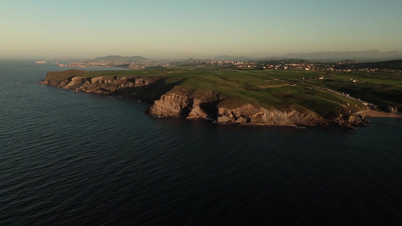 Klippekyst med grønne enge og små bebyggelser, luftfoto fra drone.