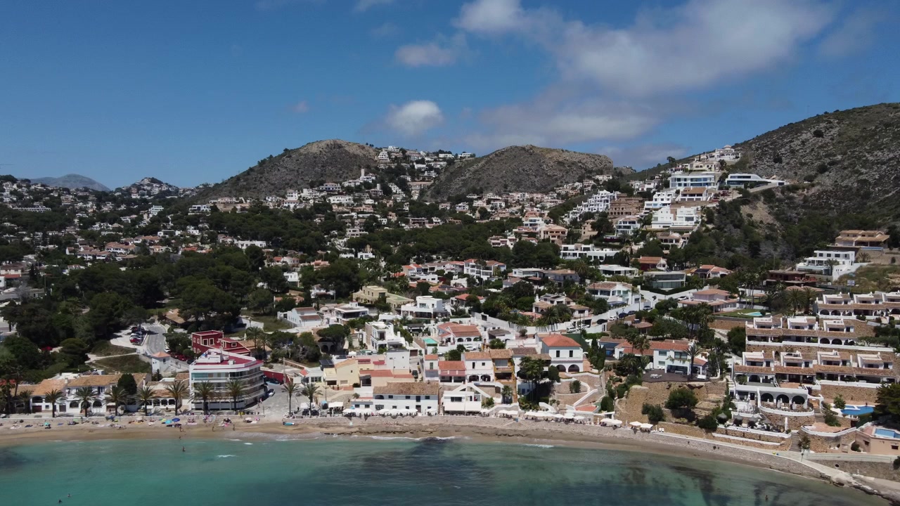 Tomada aérea de drone subindo e se afastando das pitorescas margens da praia de El Portet em Moraira, Espanha, revelando a bela costa mediterrânea.