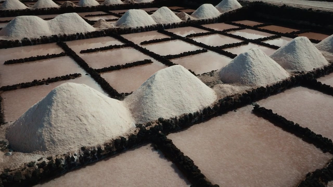 Ripresa aerea con drone di cumuli di sale alle Saline di Janubio a Lanzarote, Spagna, con vasche di sale rosa e muri in pietra vulcanica mentre il drone si muove ad arco intorno alla scena