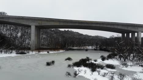 A-slow,-rising-shot-of-Page-Bridge-over-a-frozen-lake-in-Missouri,-as-snow-falls