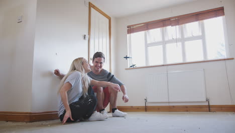 Couple-Sitting-On-Floor-In-Empty-Room-Of-New-Home-Planning-Design