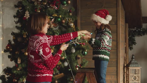 Happy-mom-and-daughter-putting-lights-on-Christmas-tree-at-home