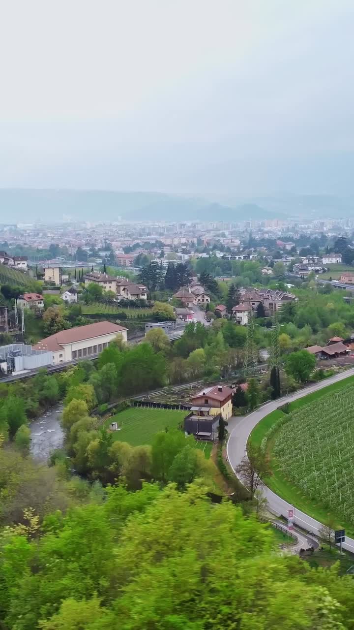 Valley city with winding river, bridge, and moving vehicle under overcast sky