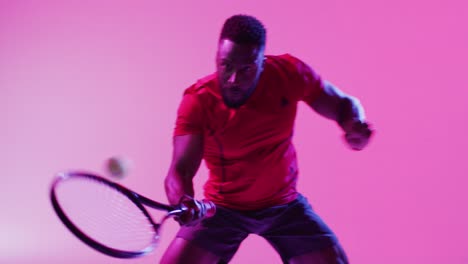 Video-of-focused-african-american-male-tennis-player-hitting-ball-on-neon-pink-lightning