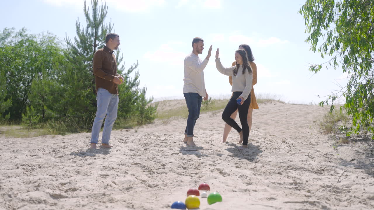 Front view of group of women and men friends playing petanque on the beach on a sunny day